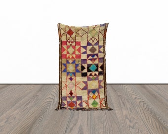 May include: A colorful Moroccan rug with a geometric pattern of squares and diamonds in shades of red, blue, green, purple, and white. The rug has a brown fringe on the edges.