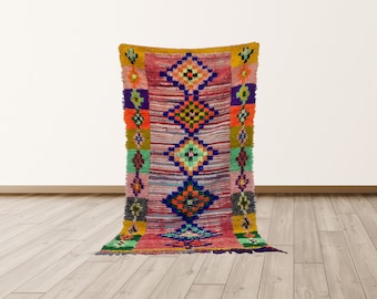 May include: A colorful Moroccan rug with a geometric pattern in shades of pink, blue, green, orange, and yellow. The rug has a fringe border and is made of wool.