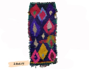 May include: A colorful Moroccan rug with a geometric pattern in shades of pink, blue, yellow, green, and purple. The rug is approximately 2.8 feet wide and 6 feet long.