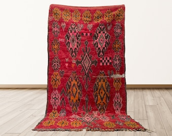 May include: A red, orange, and pink Moroccan rug with a geometric pattern. The rug has a fringe border and is made of wool.