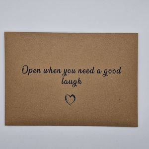 K&ouml;nnte beinhalten: Ein brauner Papierumschlag mit dem Text "Open when you need a good laugh" und einem kleinen gezeichneten Herzen.