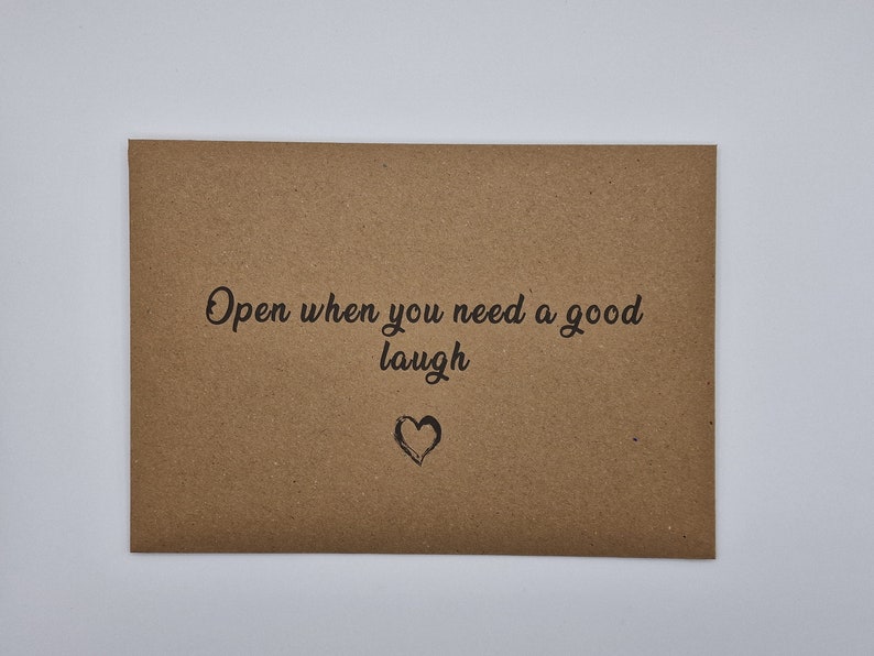 K&ouml;nnte beinhalten: Ein brauner Papierumschlag mit dem Text "Open when you need a good laugh" und einem kleinen gezeichneten Herzen.