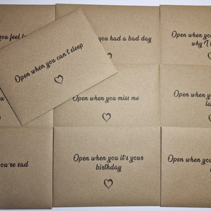 May include: A selection of brown paper envelopes with handwritten text and heart illustrations. The phrases include "Open when you feel," "Open when you can't sleep," and "Open when you're sad." Perfect for gifting.