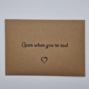 K&ouml;nnte beinhalten: Ein brauner Papierumschlag mit dem Text "Open when you're sad" und einem handgezeichneten Herzen.