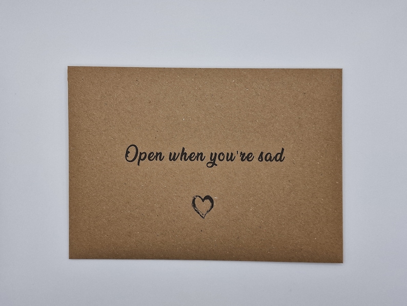 K&ouml;nnte beinhalten: Ein brauner Papierumschlag mit dem Text "Open when you're sad" und einem handgezeichneten Herzen.