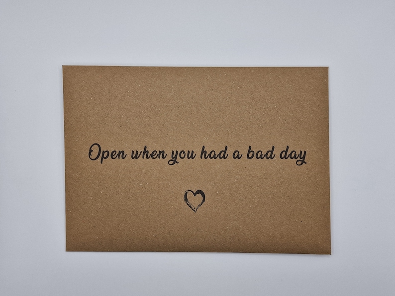 K&ouml;nnte beinhalten: Ein brauner Papierumschlag mit dem Text "Open when you had a bad day" und einem kleinen gezeichneten Herzen.