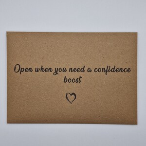 K&ouml;nnte beinhalten: Ein brauner Papierumschlag mit dem Text "Open when you need a confidence boost" und einem kleinen gezeichneten Herzen.