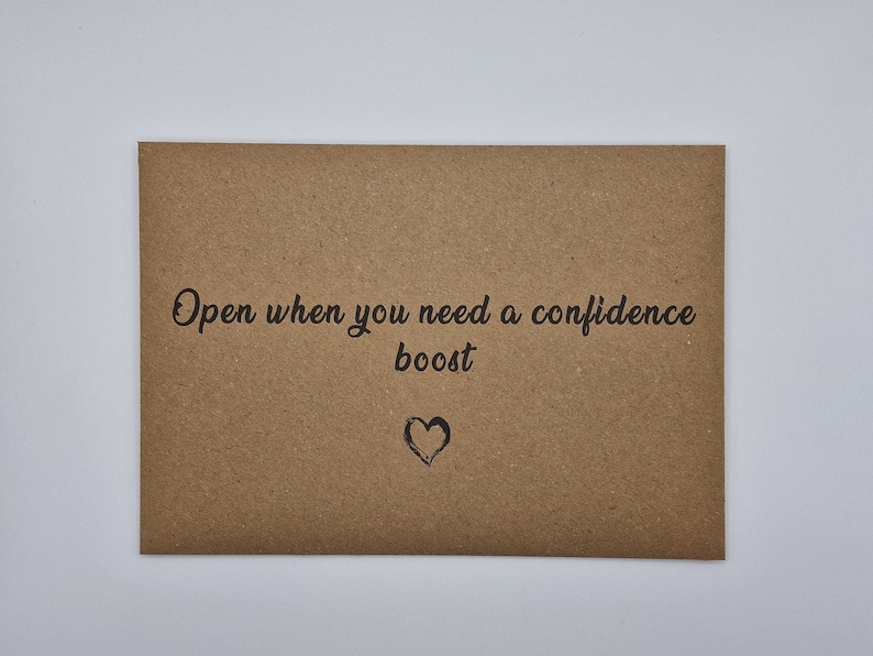 K&ouml;nnte beinhalten: Ein brauner Papierumschlag mit dem Text "Open when you need a confidence boost" und einem kleinen gezeichneten Herzen.