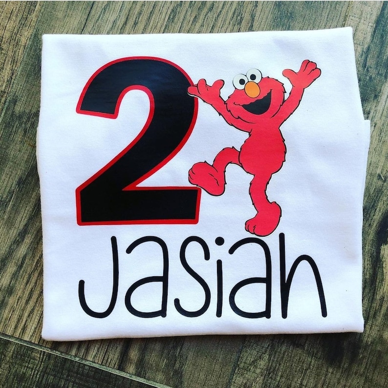 May include: White t-shirt with a black number 2 and a red Elmo character. The shirt also has the name "Jasian" written in black.
