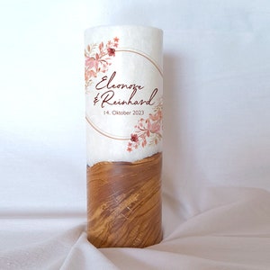 May include: A white candle with a wood base. The candle has a floral design with a gold circle and the text "Eleonore & Reinhard 14. Oktober 2023".