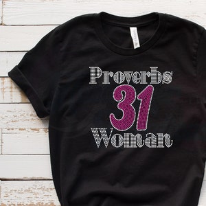 May include: Black t-shirt with a rhinestone design that says "Proverbs 31 Woman". The number 31 is pink.
