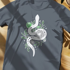 May include: A dark gray t-shirt with a white graphic of a snake curled around flowers and moons. The flowers are green and white.