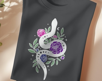 Puede incluir: Una camiseta gris oscuro con un diseño de serpiente blanca. La serpiente está enroscada alrededor de un grupo de flores moradas y rosas. El diseño está rodeado de pequeñas estrellas blancas y lunas crecientes.