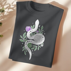 May include: A dark gray t-shirt with a white snake design. The snake is curled around a cluster of flowers and leaves. The flowers are purple and white.