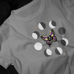 Pode incluir: Uma camiseta cinza com uma borboleta roxa e amarela e um círculo de oito luas em diferentes fases.