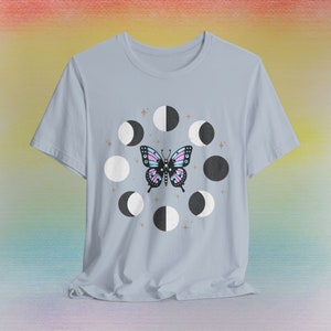 Könnte beinhalten: Ein hellblaues T-Shirt mit einem Motiv eines Schmetterlings und einem Kreis aus Monden in Schwarz und Weiß.