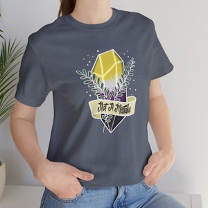 May include: A dark blue t-shirt with a yellow, purple, and white crystal design. The crystal is surrounded by green leaves and a banner that reads "Not A Mistake".