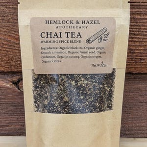 May include: A kraft paper bag of Chai Tea from Hemlock & Hazel Apothecary. The label reads "Chai Tea Warming Spice Blend" with a cinnamon stick illustration. The ingredients include organic black tea, ginger, cinnamon, fennel seed, cardamom, nutmeg, pepper, and cloves. Net weight: 2 oz.