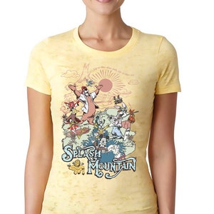 May include: A yellow t-shirt with a vintage-style illustration of characters from Splash Mountain. The illustration features a bear, rabbit, and other characters in a whimsical setting. The text "Splash Mountain" is printed in blue and white.