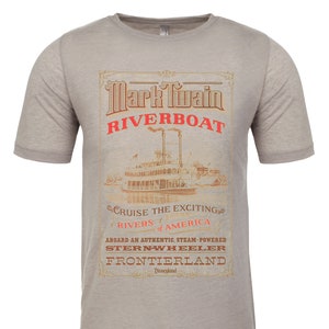 May include: A gray t-shirt with a vintage-style illustration of the Mark Twain Riverboat at Disneyland. The text reads "Mark Twain Riverboat, Cruise the Exciting Rivers of America, Aboard an Authentic, Steam-Powered Stern-Wheeler, Frontierland, Disneyland."