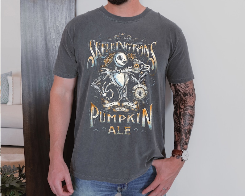 Puede incluir: Una camiseta gris oscuro con un gr&aacute;fico de estilo vintage de un esqueleto sosteniendo una jarra de cerveza. El gr&aacute;fico incluye el texto "Skeligtons" y "Pumpkin Ale".