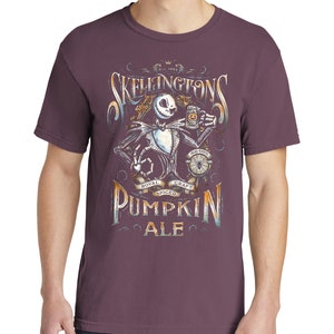 Puede incluir: Una camiseta morada con un gr&aacute;fico de Jack Skellington de Pesadilla Antes de Navidad sosteniendo una jarra de cerveza. El gr&aacute;fico incluye el texto "Skellington's Pumpkin Ale" y "Royal Spiced Craft".