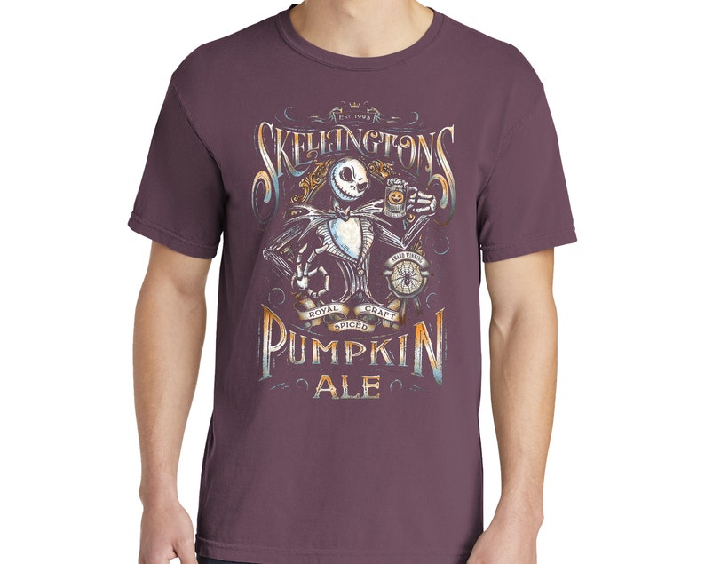 Puede incluir: Una camiseta morada con un gr&aacute;fico de Jack Skellington de Pesadilla Antes de Navidad sosteniendo una jarra de cerveza. El gr&aacute;fico incluye el texto "Skellington's Pumpkin Ale" y "Royal Spiced Craft".