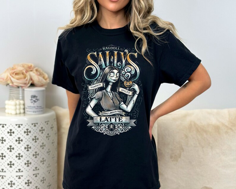 Puede incluir: Camiseta negra con un gr&aacute;fico de Sally de Pesadilla antes de Navidad. El gr&aacute;fico muestra a Sally sosteniendo un latte de calabaza especiado y el texto "Ragdoll Sally's Pumpkin Spiced Latte Frogg's Breath Free".