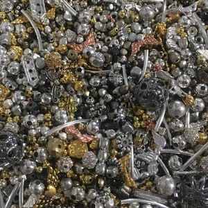 May include: A large assortment of silver, gold, and black beads and charms. The beads are of various shapes and sizes, including round, square, and heart-shaped. The charms are also of various shapes and sizes, including wings, flowers, and stars.