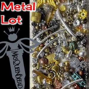 May include: A close-up image of a clear plastic container filled with a variety of metal beads and charms. The beads are in various shapes, sizes, and colors, including gold, silver, copper, and turquoise. The container is labeled "EXAMPLE 2oz Metal Lot" and "Each Lot Contains 2.6oz!"