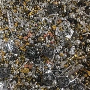 May include: A large assortment of silver, gold, and black metal beads and charms. The beads are of various shapes and sizes, including round, square, and heart-shaped. The charms are also of various shapes and sizes, including butterflies, flowers, and stars.