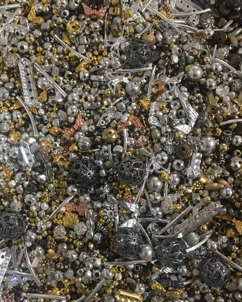 May include: A large assortment of silver, gold, and black metal beads and charms. The beads are of various shapes and sizes, including round, square, and heart-shaped. The charms are also of various shapes and sizes, including butterflies, flowers, and stars.
