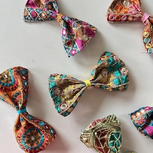 Puede incluir: Seis lazos de tela coloridos con adornos de espejo. Los lazos son en tonos de rosa, naranja, amarillo, verde y azul.