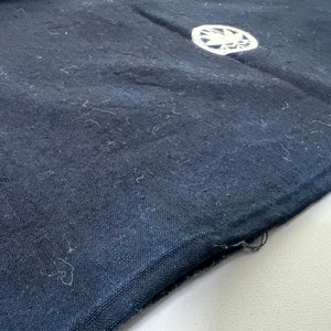 Könnte beinhalten: Ein dunkelblauer Stoff mit einem weißen runden Fleck, der ein stilisiertes Design zeigt. Der Stoff hat eine strukturierte Oberfläche und ist leicht zerknittert.