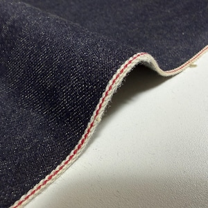 Peut inclure: Un morceau de tissu en jean bleu indigo foncé présentant un bord selvedge distinct. Le bord est fini avec une bordure blanche nette et une fine ligne rouge vibrante courant parallèlement sur toute la longueur du matériau en tissu plié.