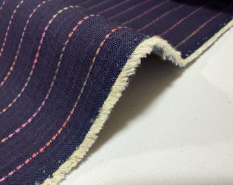 May include: Close-up of a navy blue fabric with vertical, colorful pinstripes. The fabric has a textured appearance and a frayed edge. The pinstripes are in shades of red, orange, pink, and green.