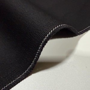 以下が含まれることがあります： 織り目が特徴的な、折りたたまれた黒い布のクローズアップ。端は白いジグザグステッチで仕上げられています。布はわずかに湾曲しており、その厚さと質感がわかります。