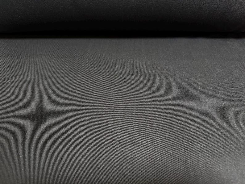 Puede incluir: Primer plano de un rollo de tela negra. La tela tiene una sutil textura acanalada diagonal, creando profundidad visual. El color es negro s&oacute;lido y profundo, con un ligero brillo.