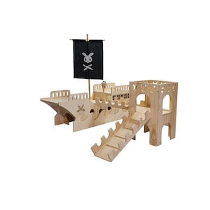 May include: A wooden pirate ship playset with a black flag featuring a skull and crossbones. The ship has a ramp and a tower with a cutout window. The playset is made of natural wood.