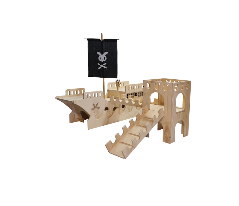 May include: A wooden pirate ship playset with a black flag featuring a skull and crossbones. The ship has a ramp and a tower with a cutout window. The playset is made of natural wood.