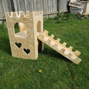 May include: A wooden castle playset with a slide and a heart-shaped window. The castle is made of plywood and has a stone-like texture. The slide is made of wood and has a smooth surface. The playset is painted in a light brown color.