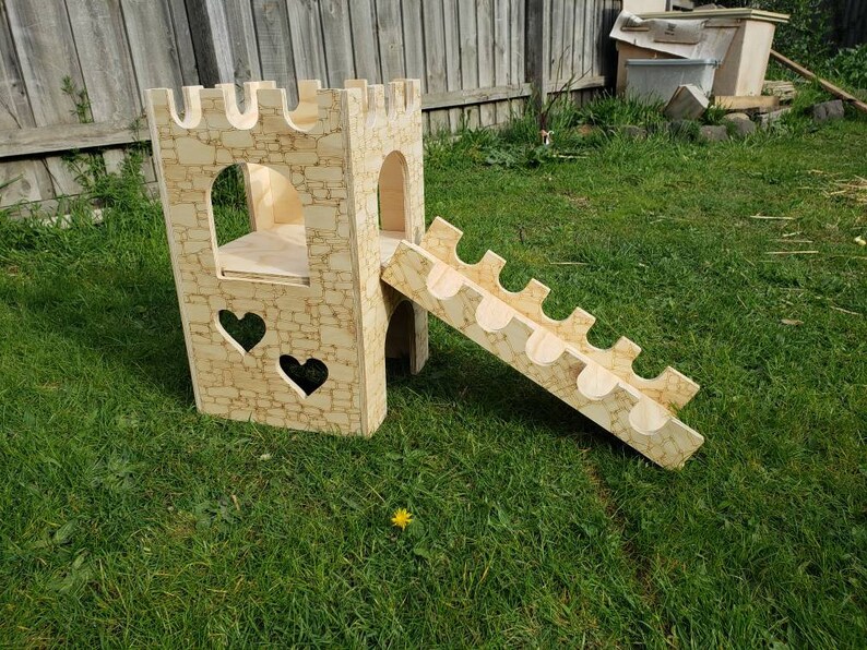 May include: A wooden castle playset with a slide and a heart-shaped window. The castle is made of plywood and has a stone-like texture. The slide is made of wood and has a smooth surface. The playset is painted in a light brown color.