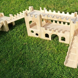 May include: A wooden castle playset with two slides and a bridge. The castle is made of plywood and has a natural wood finish. The slides are both made of plywood and have a natural wood finish. The bridge is also made of plywood and has a natural wood finish.
