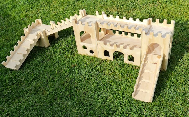 May include: A wooden castle playset with two slides and a bridge. The castle is made of plywood and has a natural wood finish. The slides are both made of plywood and have a natural wood finish. The bridge is also made of plywood and has a natural wood finish.