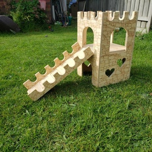 May include: A wooden castle playset with a slide and heart cutouts. The castle is made of light brown wood and has a stone-like texture. The slide is made of the same wood and has a curved shape.