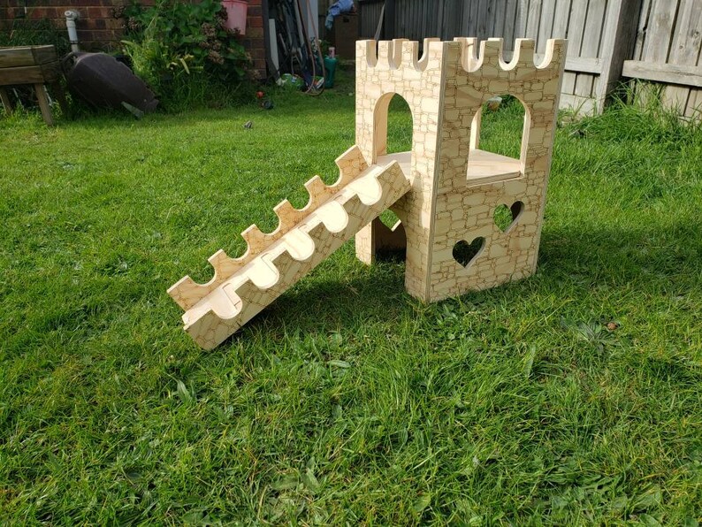 May include: A wooden castle playset with a slide and heart cutouts. The castle is made of light brown wood and has a stone-like texture. The slide is made of the same wood and has a curved shape.