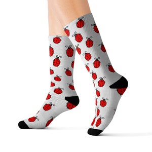 May include: A pair of white socks with a red ladybug pattern. The socks are shown on a model's legs.