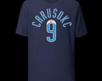 May include: Navy blue t-shirt with the name "CARUSOKC" arched across the top in light blue lettering. Below the name is a light blue number "9" with a white outline. The shirt features a basketball graphic and the letters "OKC".