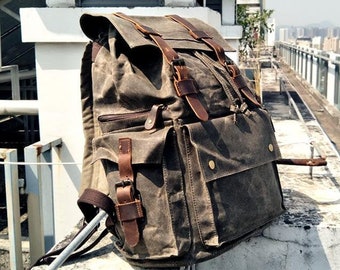 May include: A brown canvas backpack with leather straps and buckles. The backpack has multiple pockets and a flap closure.