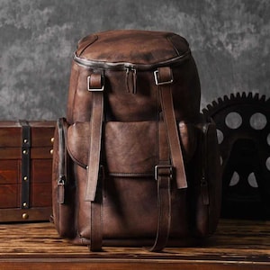 May include: A brown leather backpack with multiple pockets and buckles. The backpack has a distressed look and is made of high-quality leather.